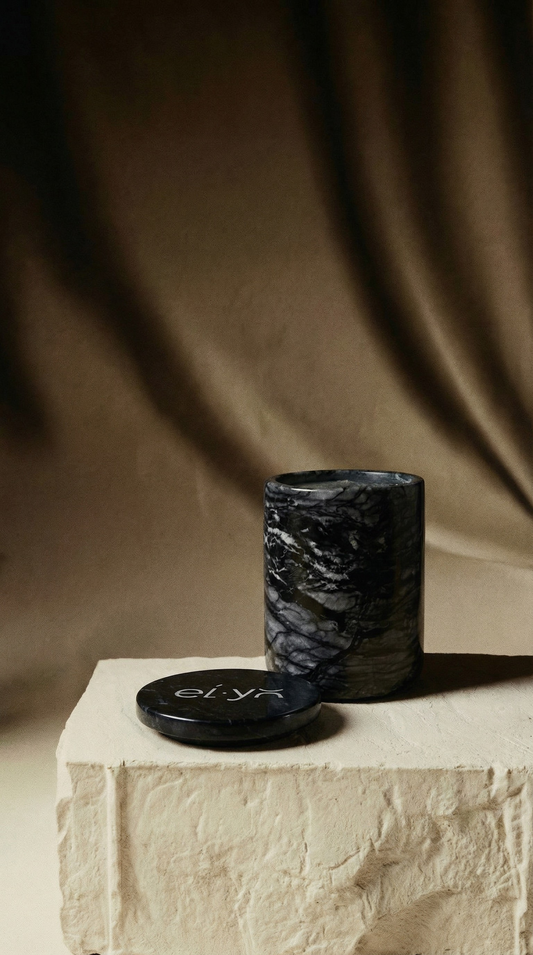 Marble-textured candle on a stone surface with a beige curtain background